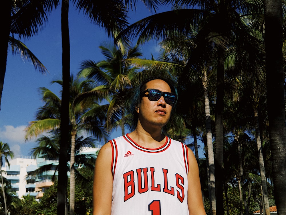 man wearing Chicago Bulls jersey with sunglasses surrounded by palm trees during daytime