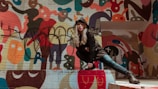 Street-style shot of a model posing against an orange wall covered in black graffiti art.