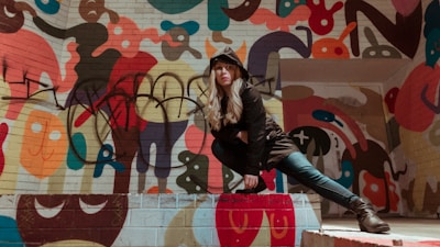 Street-style shot of a model posing against an orange wall covered in black graffiti art.