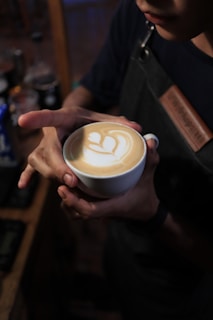 Close-up of a perfectly crafted cappuccino with latte art on top, held in a customer's hand.