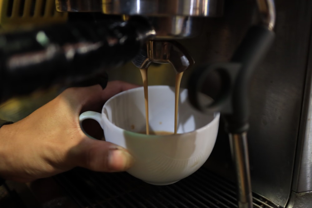 personne versant un liquide brun sur une tasse de thé blanche