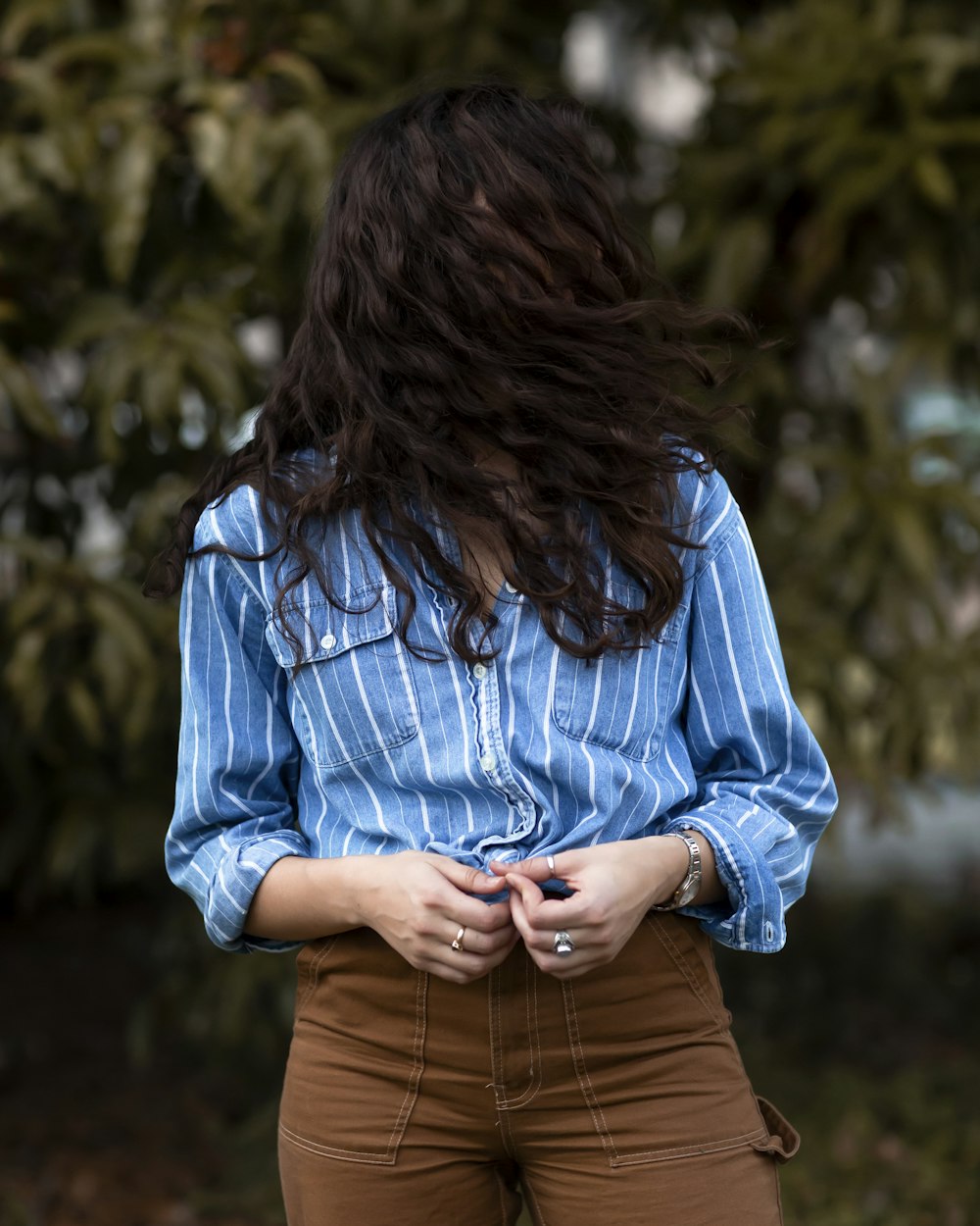 woman's face covered with his hair holding blue and white stripe dress shirt