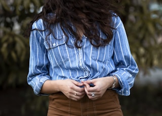 woman's face covered with his hair holding blue and white stripe dress shirt