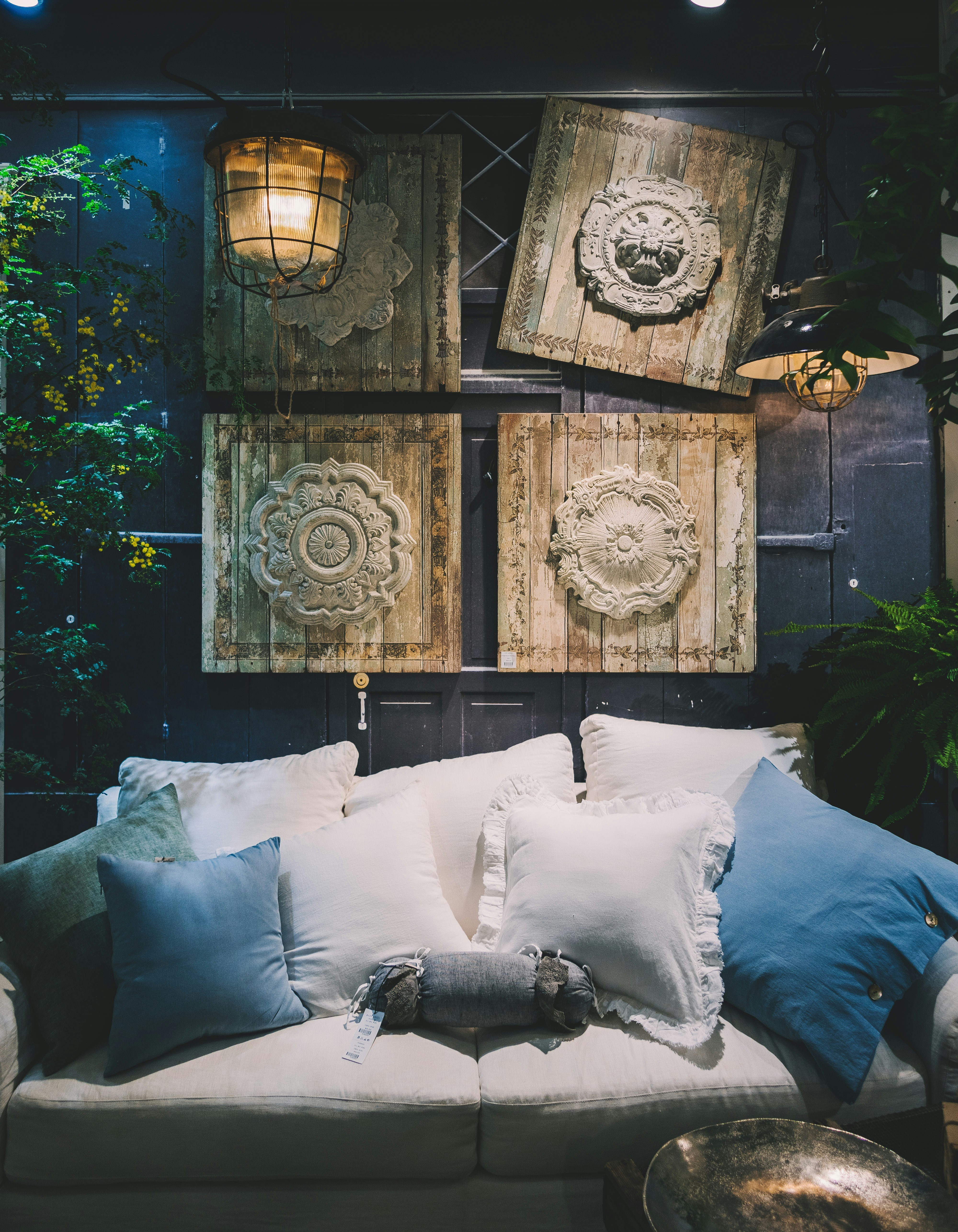 Cozy lounge scene with four carved wooden panels arranged above a plush white sofa, accented by blue and white cushions and warm ambient lighting.