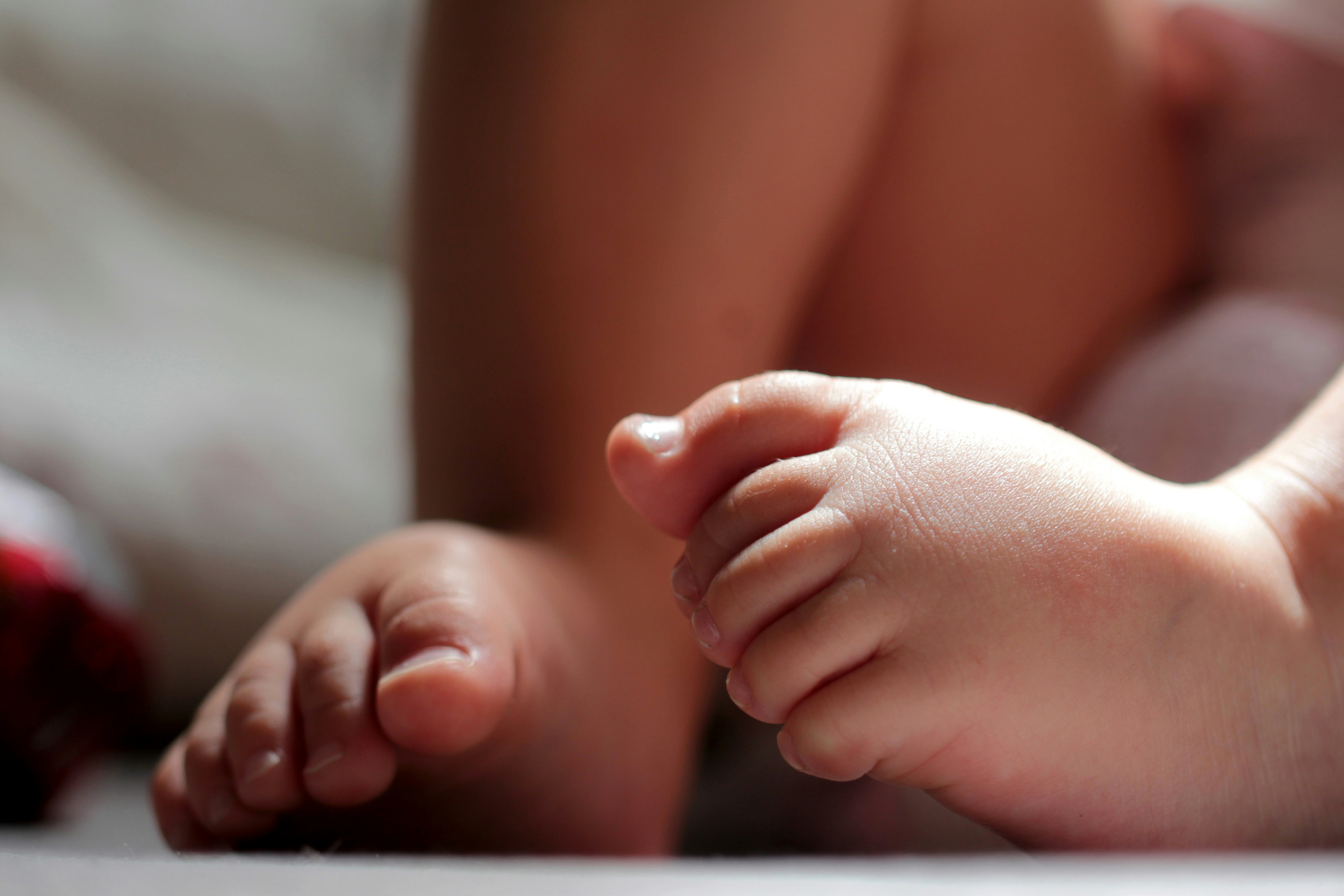 Soft baby clothes and tiny shoes on dark background, gentle dim studio lighting