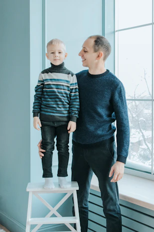 A smiling parent helping their child adjust the seat height on a tinywheelz bike in a bright, airy living room.
