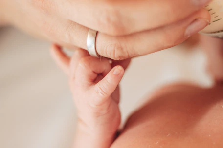 Close-up photo of a baby's hand holding a parent's finger during a baptism ceremony.