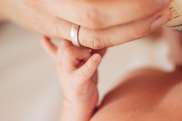 Close-up of a baby's tiny hand holding a mother's finger in soft natural light.