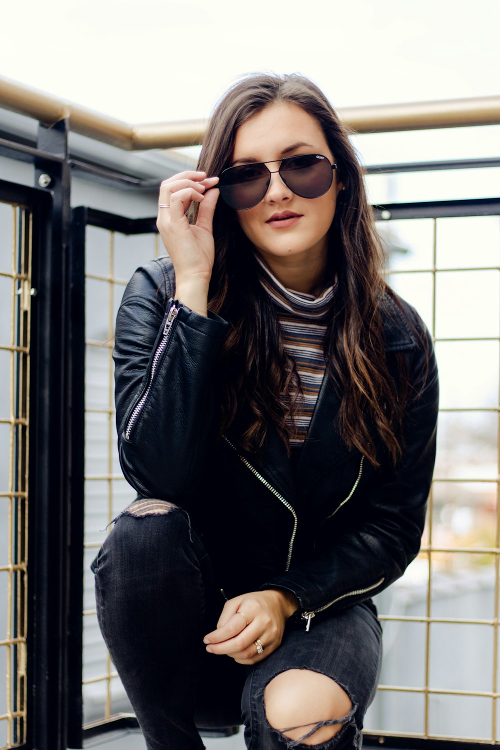 sitting woman wearing black leather jacket and distressed black denim jeans right hand holding sunglasses