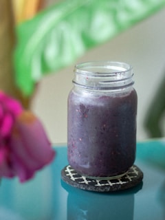 A close-up of a colorful, nutrient-rich smoothie poured into a mason jar with fresh fruit around it.