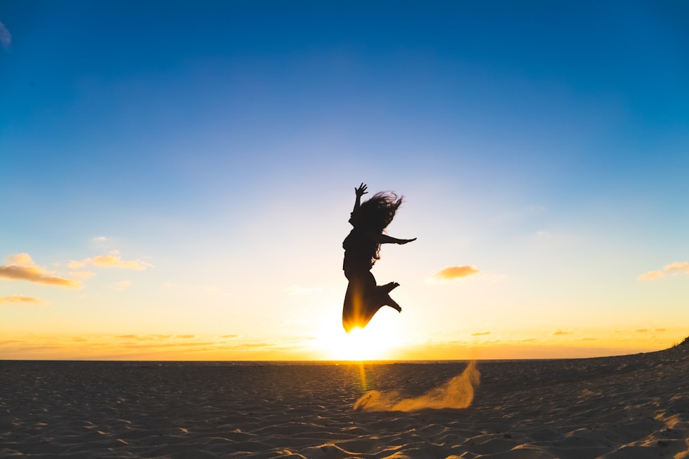 woman leaping at sand during sunset