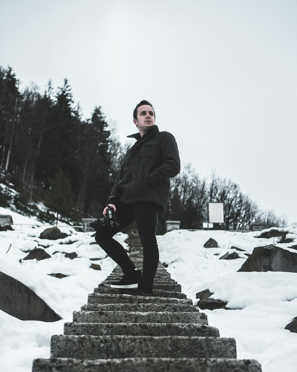 man wearing black jacket standing on stair near the tree