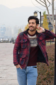 A man dressed in a cozy sweater, smiling while walking in a park.