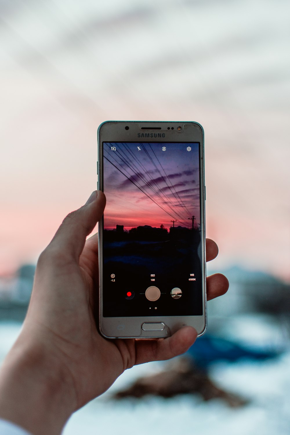 person taking photo of black electric wire under red cloudy sky