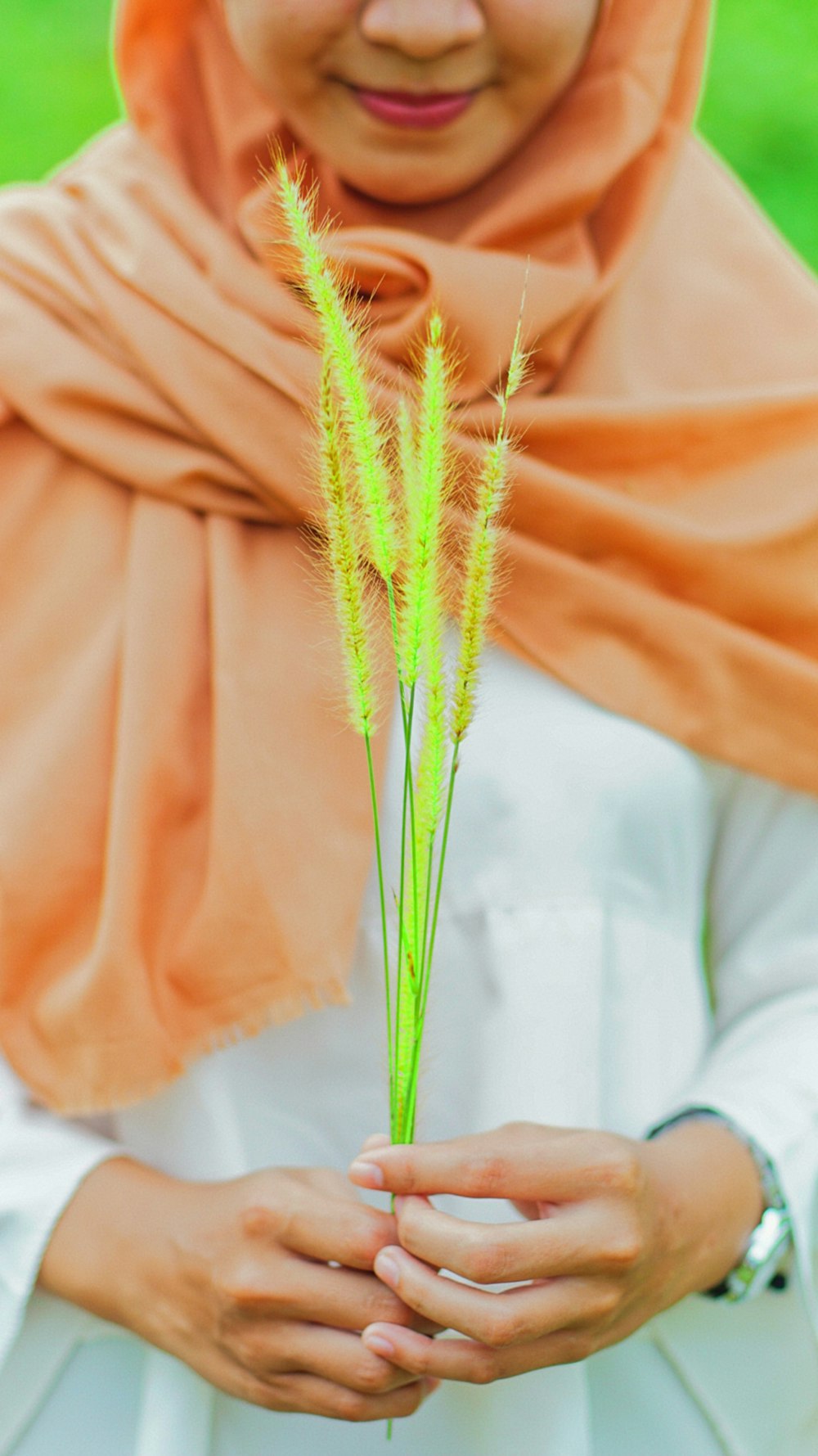 woman wearing orange hijab holding grass flowers