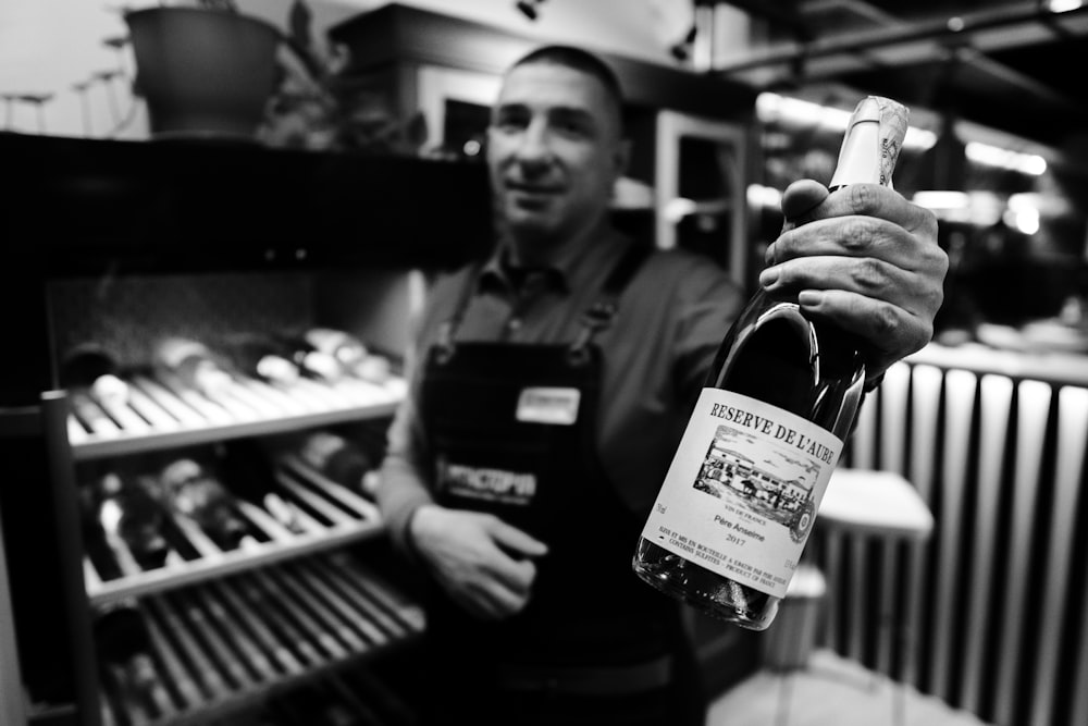 man holding wine bottle beside refrigerator