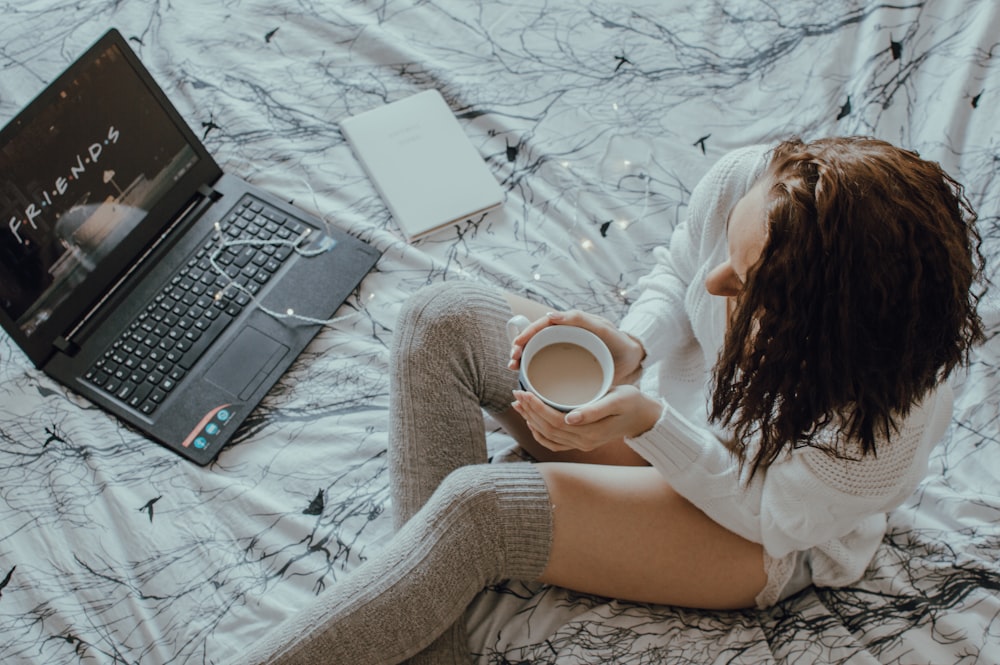 woman holding filled ceramic mug watching video on laptop