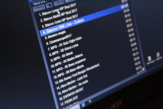 A computer screen displaying a list of audio tracks with their titles, durations, and file formats. The display is predominantly dark, creating a high contrast with the white and blue text.