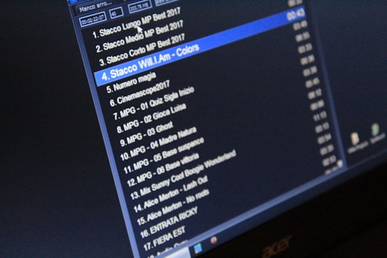 A computer screen displaying a list of audio tracks with their titles, durations, and file formats. The display is predominantly dark, creating a high contrast with the white and blue text.
