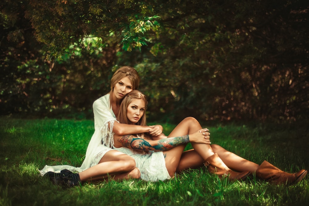two woman sitting on ground hugging near tree