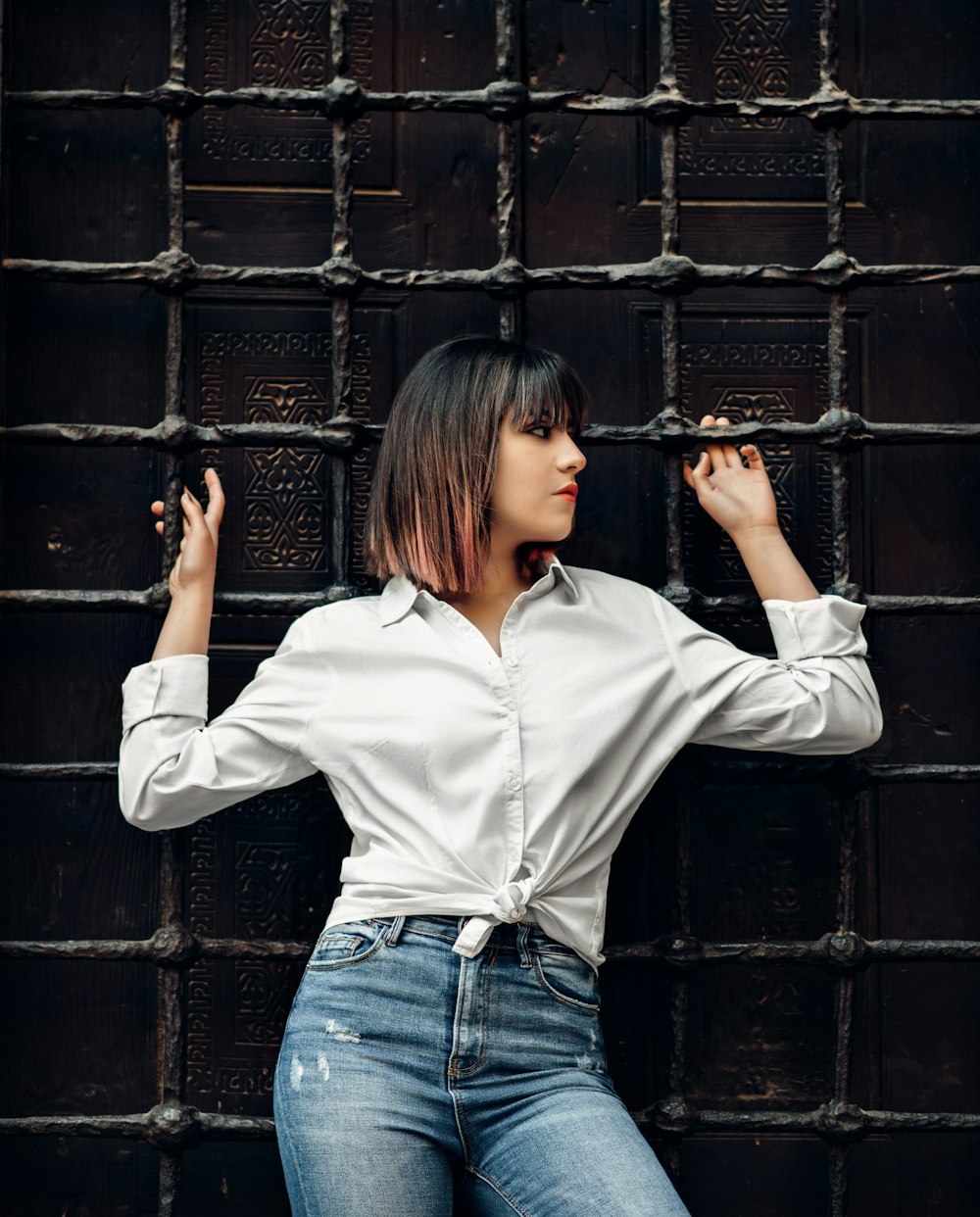 woman in white dress shirt leaning and holding on metal mesh wall