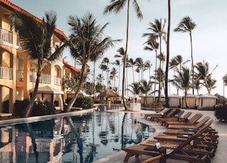 brown wooden lounge chairs near pool surrounded by palm trees