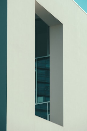 A modern architectural structure with clean lines and a minimalistic design. The building features large glass windows set within smooth, light-colored walls, contrasting with the deep shadows cast by the angular shapes.