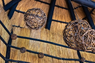 A series of spherical wicker lampshades hang from the ceiling, which is made of straw with wooden beams intersecting across it. The intricate weaving of the lampshades contrasts with the natural texture of the straw, creating an earthy and rustic aesthetic.