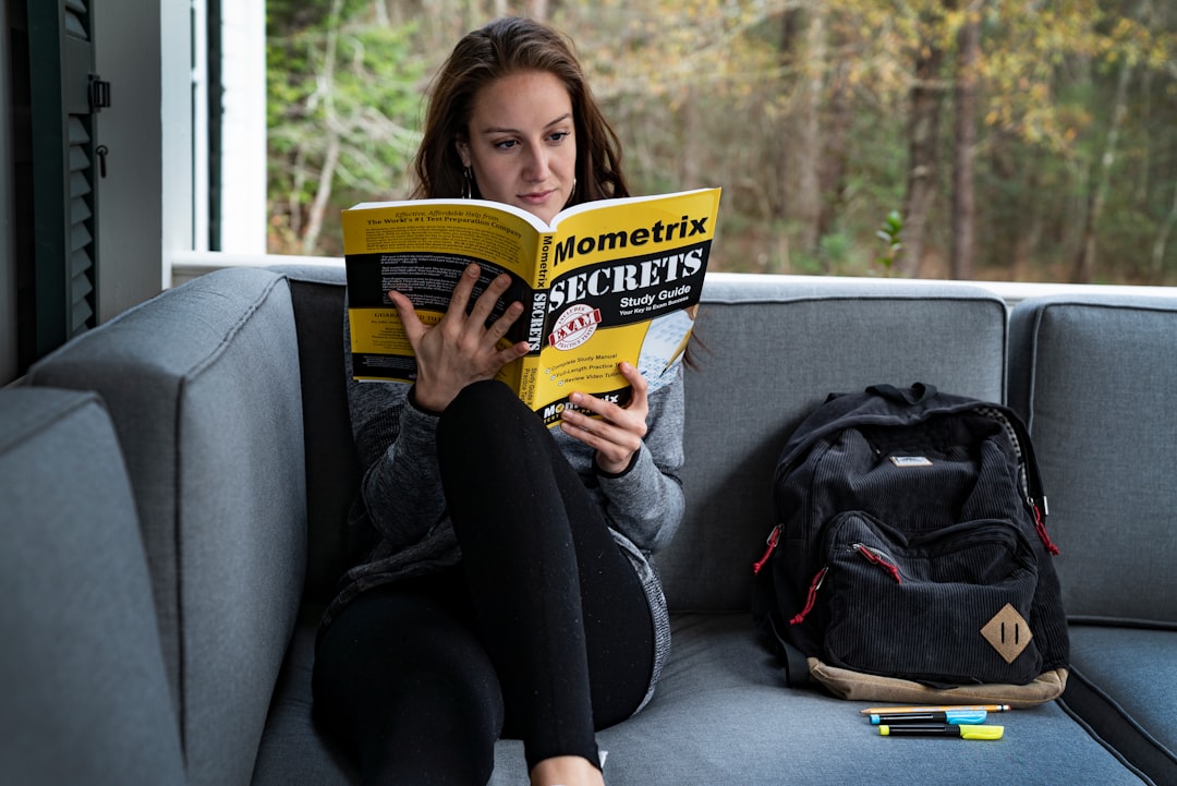 woman sitting on sofa beside bag while reading,