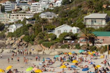 people sun bathing and standing on seashore during daytime