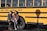 Two people are standing in front of a yellow school bus with the text 'County Career & Technical Center' written on its side. Both individuals are wearing casual clothing and are posed next to the bus shadow on the ground.
