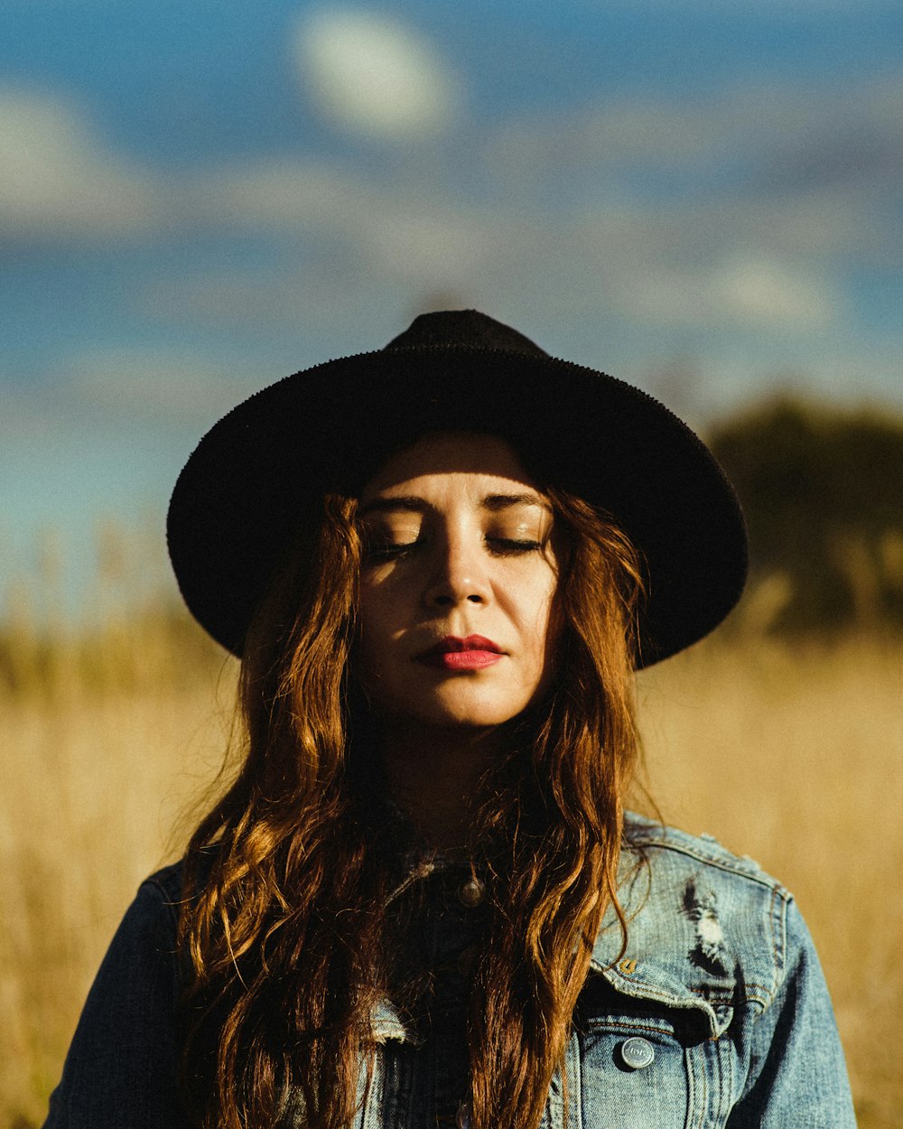 selective focus photography of woman closing her eyes wearing black sun hat and blue denim jacket
