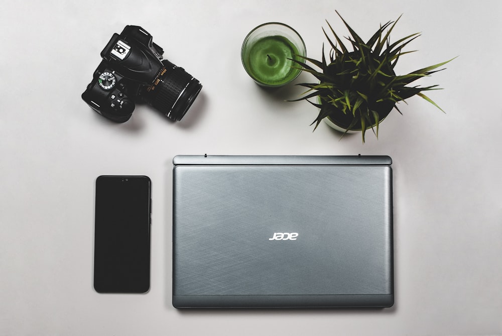 grey Acer laptop beside black smartphone and black DSLR camera