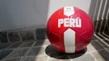 A red and white soccer ball with the word 'PERÚ' printed on it rests on a tiled floor with shadows cast from nearby bars.