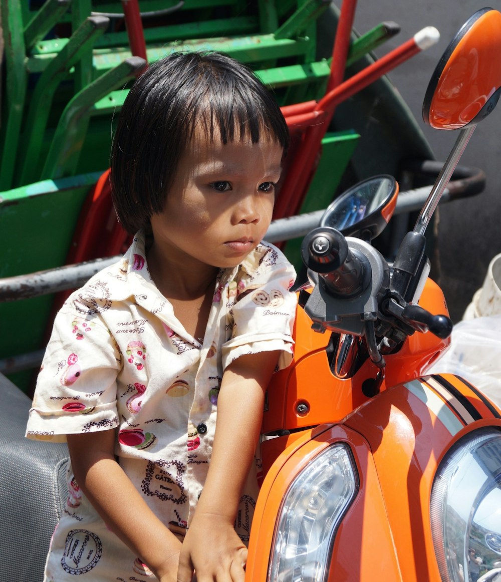 child in white top leaning by motor scooter at daytime