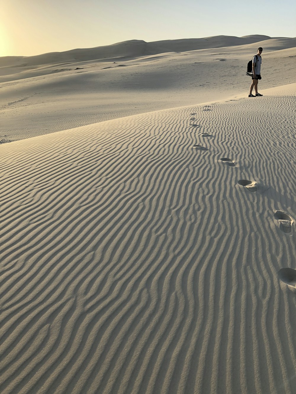 man in white t-shirt leaving footprints on sand covered field during daytime