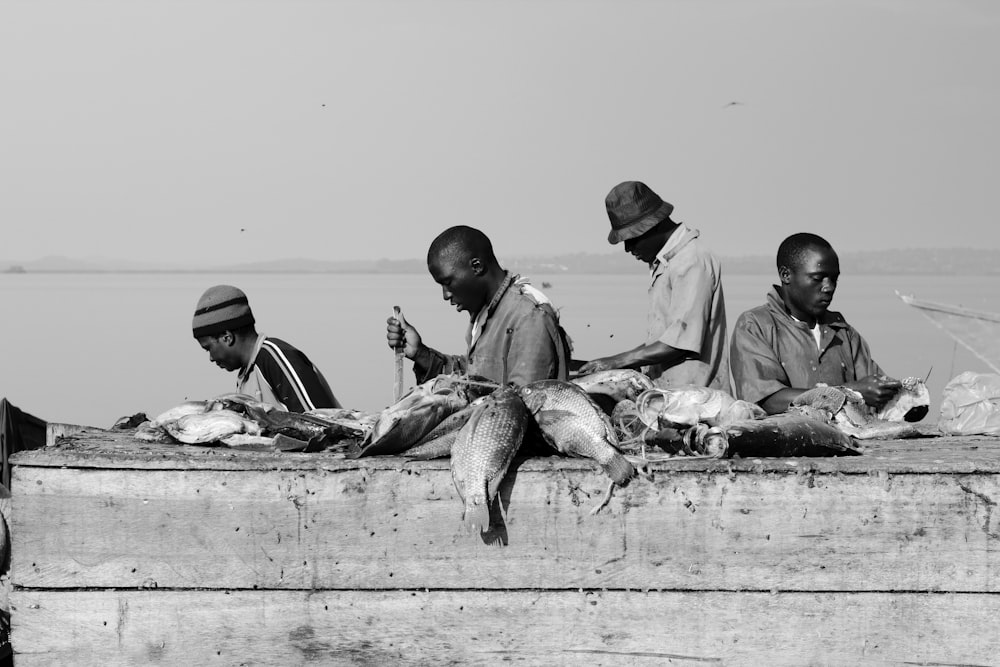 grayscale photography of four men slicing fish