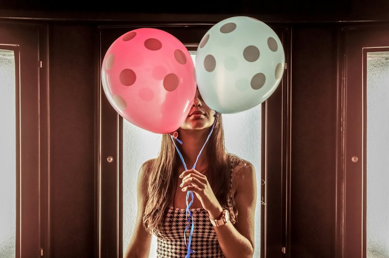 Hands holding pink and blue balloons