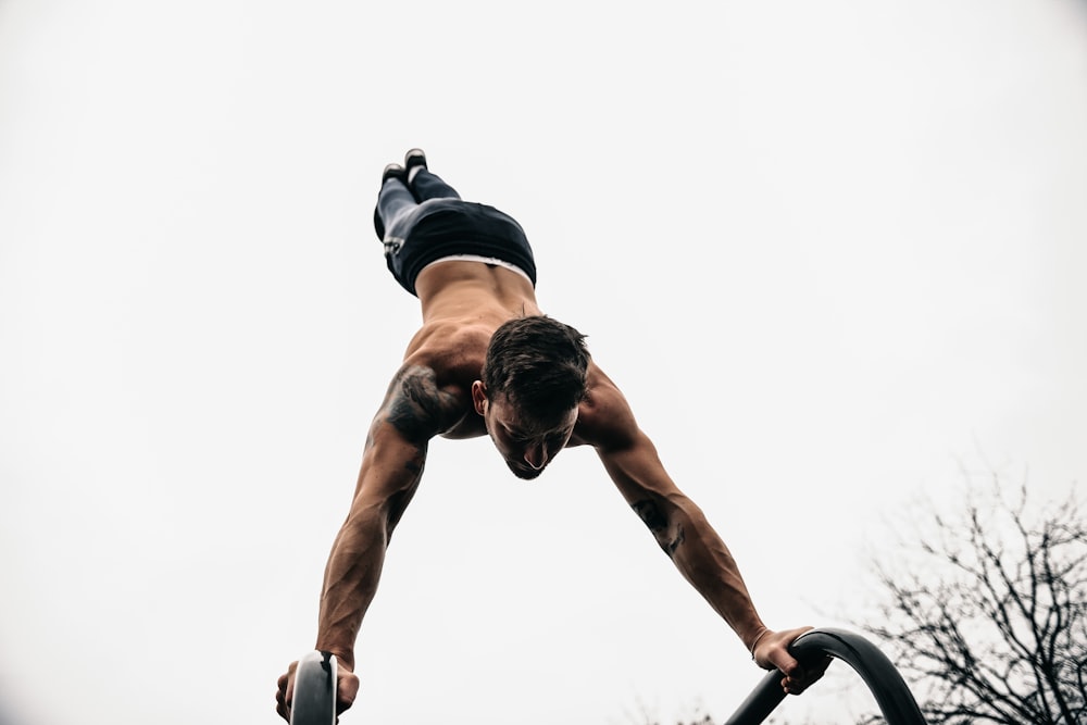 topless man doing hand stand on metal bars