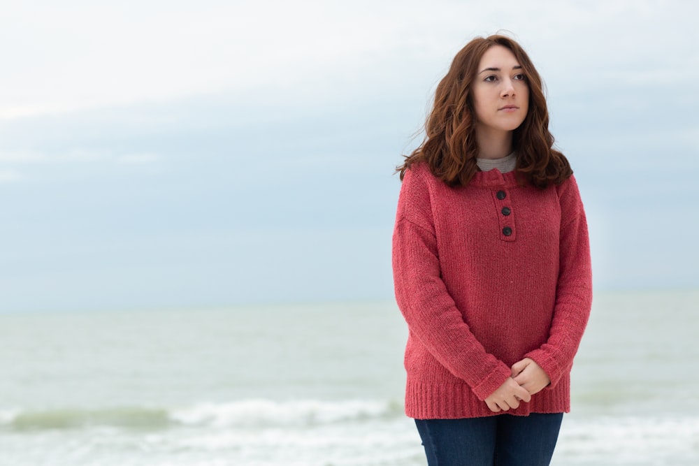 standing woman wearing red sweater and blue denim bottoms during daytime