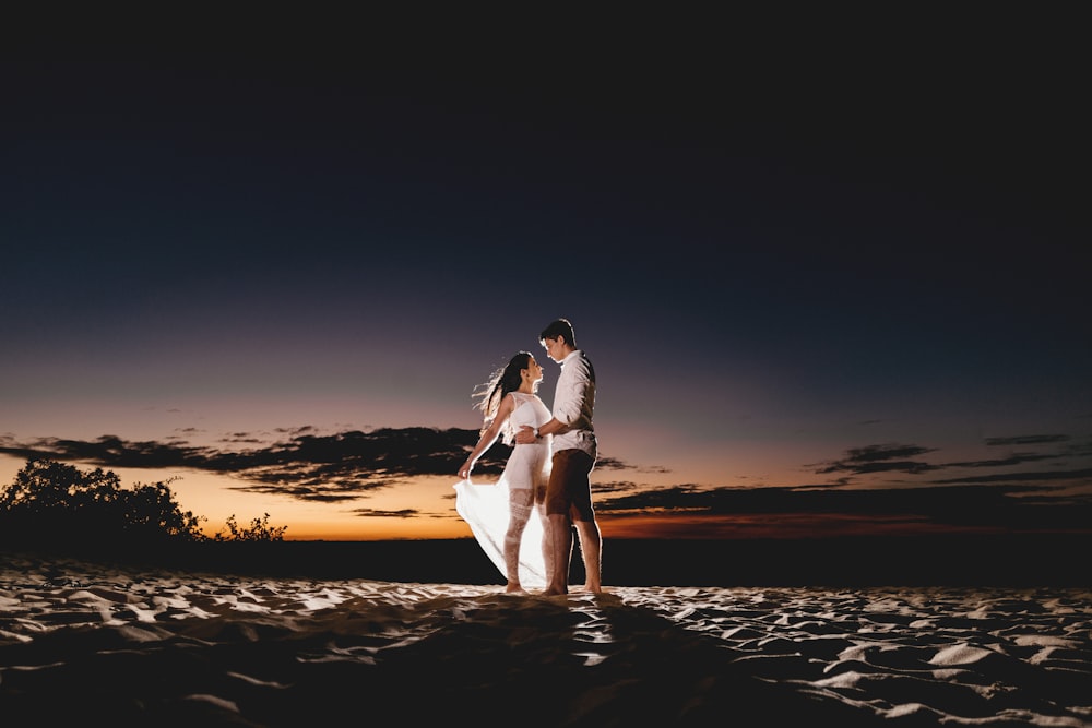 Casal em pé na areia da praia durante a hora dourada