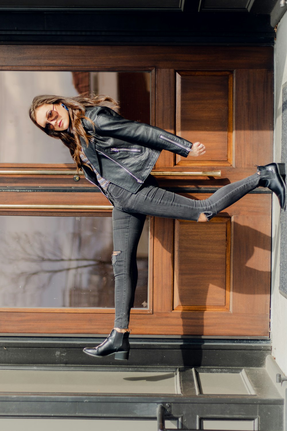 a woman in black jacket and jeans standing on a ledge