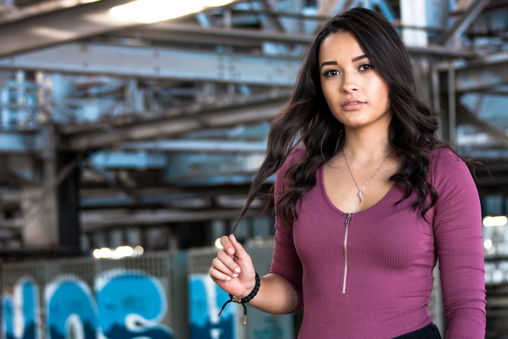 woman wearing purple half-zip long-sleeved shirt with right hand holding tip of hair