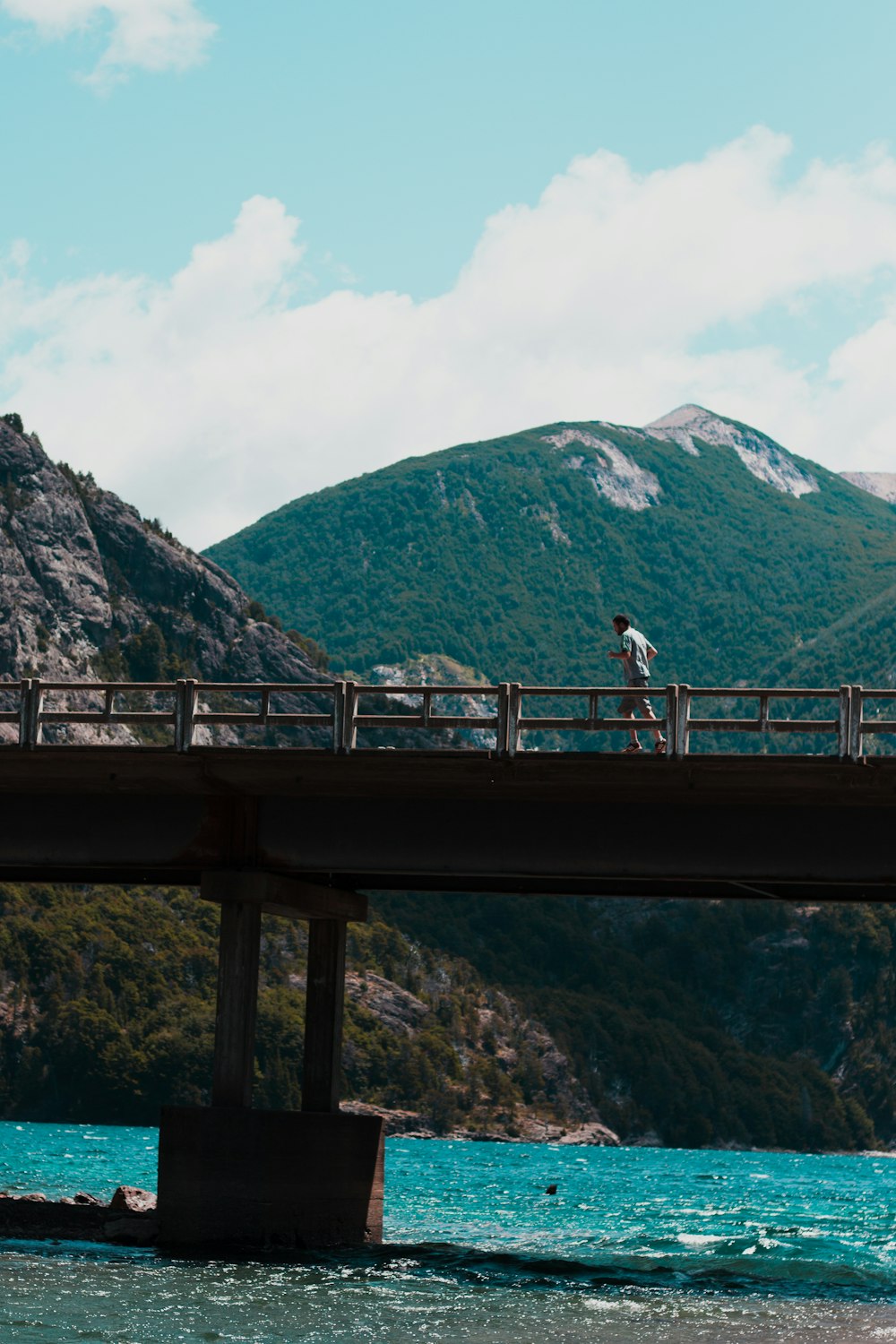 man running on concrete walk bridge above body of water during daytime