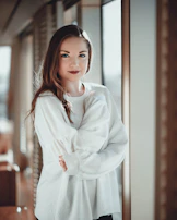 Model wearing a cozy, earth-toned sweater standing in natural light near a window.