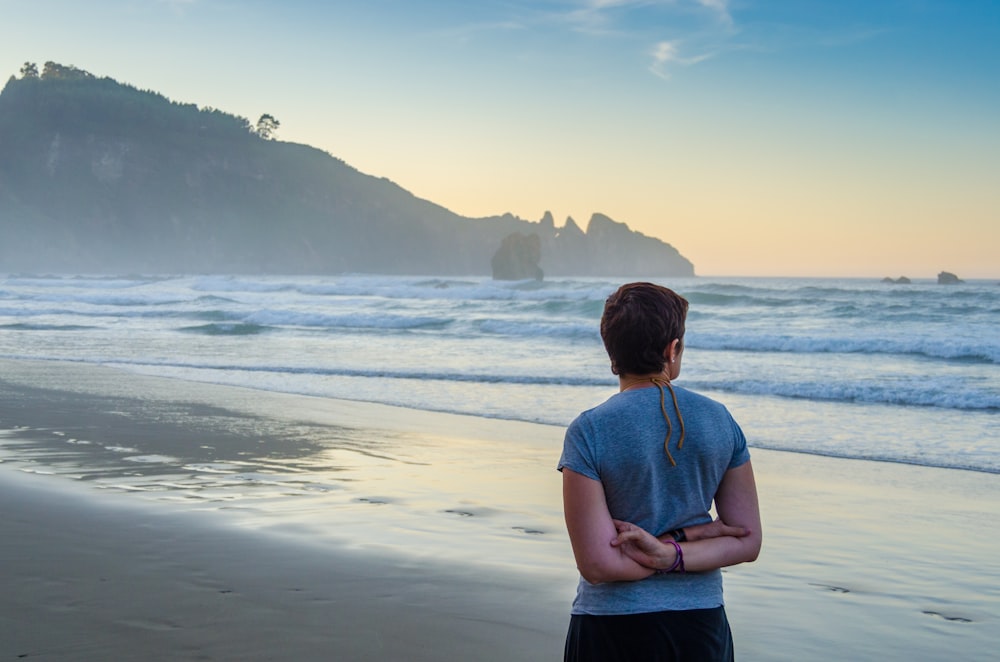 pessoa de camiseta azul colocando as duas mãos nas costas enquanto está em pé na praia