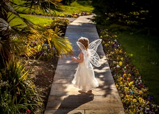 girl wearing angel costume standing on wooden pathway