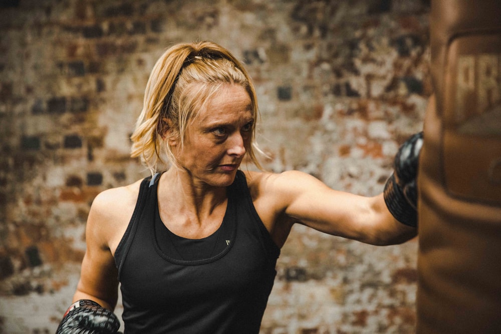 woman in black tank top punching brown heavy bag