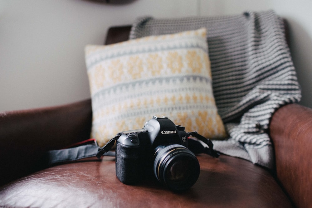 appareil photo reflex numérique Canon noir sur canapé en cuir marron