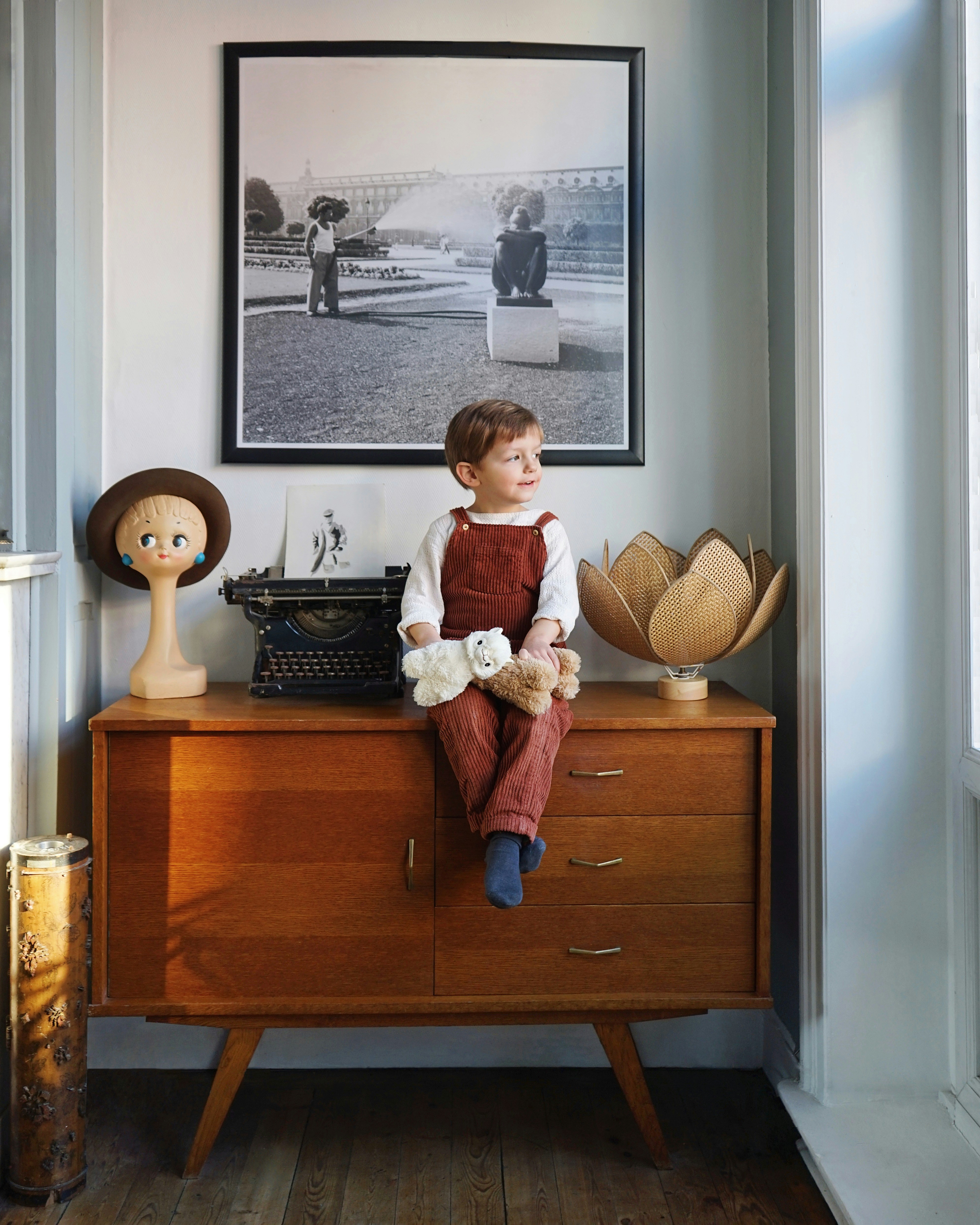 boy wearing red overalls sitting on brown wooden drawer